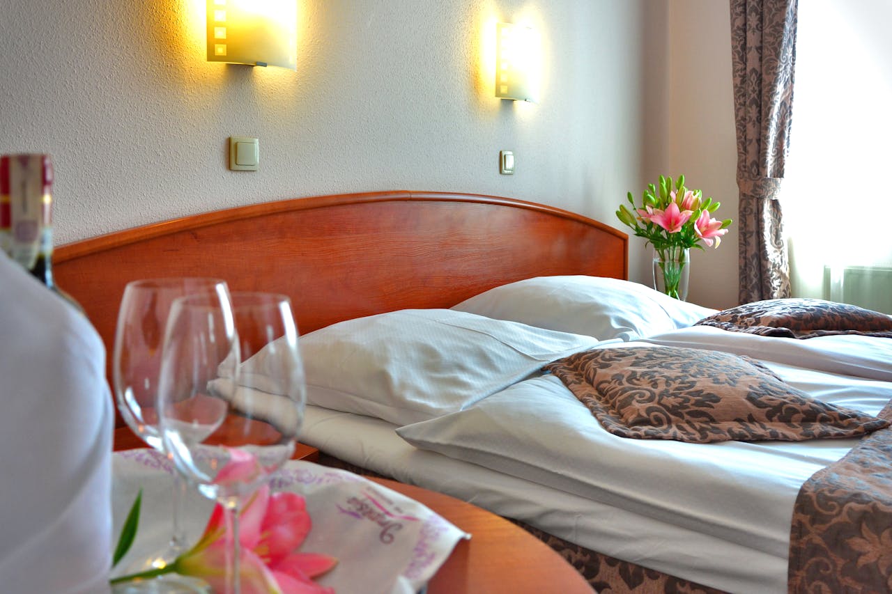 Elegant hotel room featuring a cozy bed, wine glasses, and floral decor, creating a welcoming atmosphere.